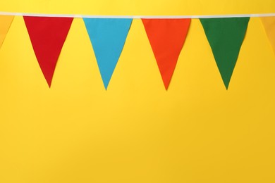 Bunting with colorful triangular flags on yellow background, space for text