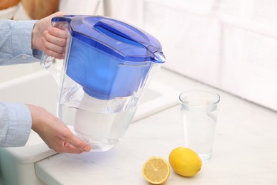 Photo of Woman with water filter jug in kitchen, closeup