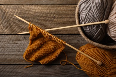 Photo of Soft colorful yarns, knitting and needles on wooden table, top view