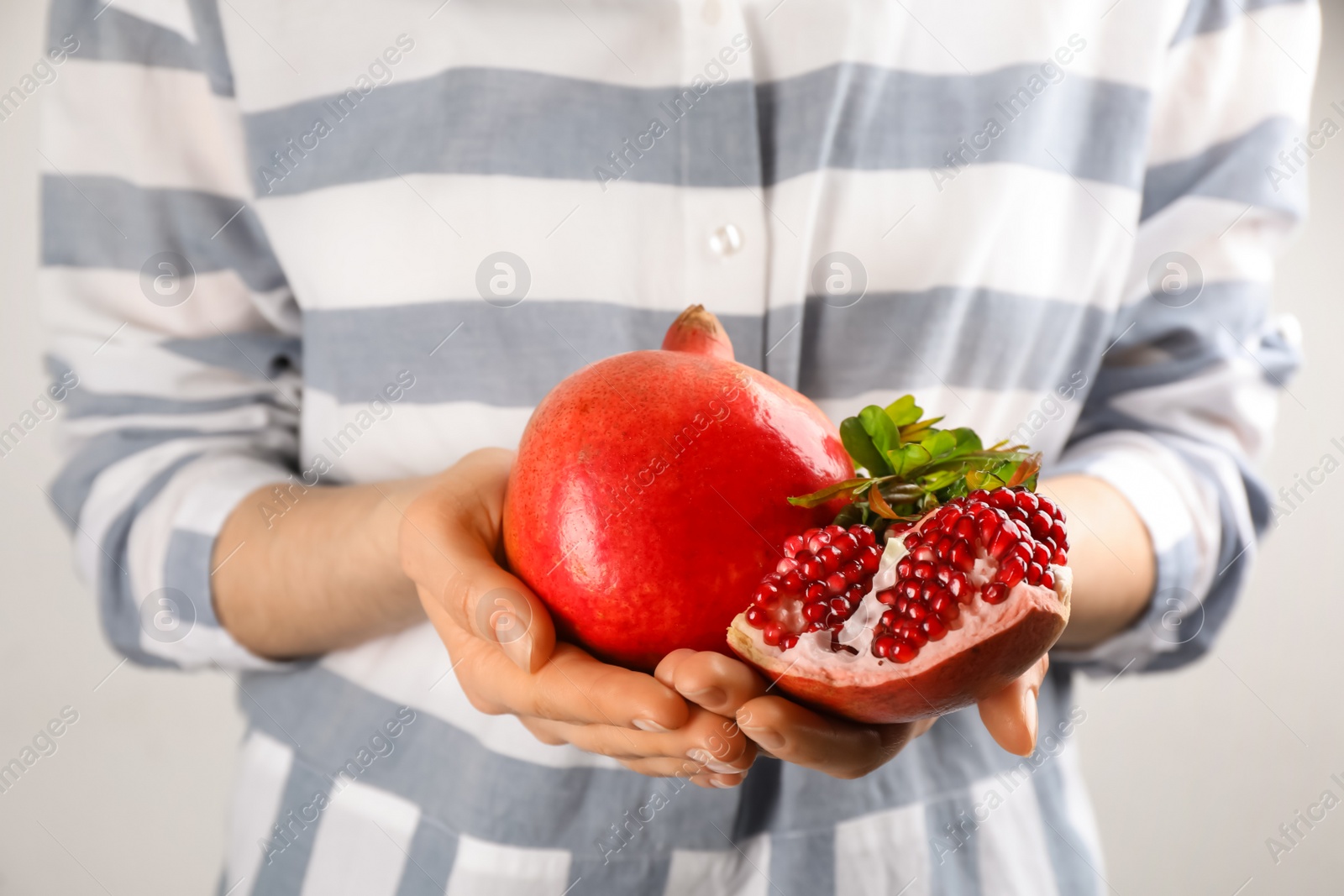 Photo of Woman holding ripe pomegranates on light background, closeup