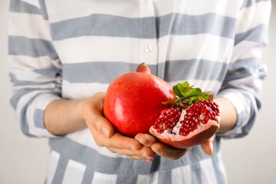 Woman holding ripe pomegranates on light background, closeup