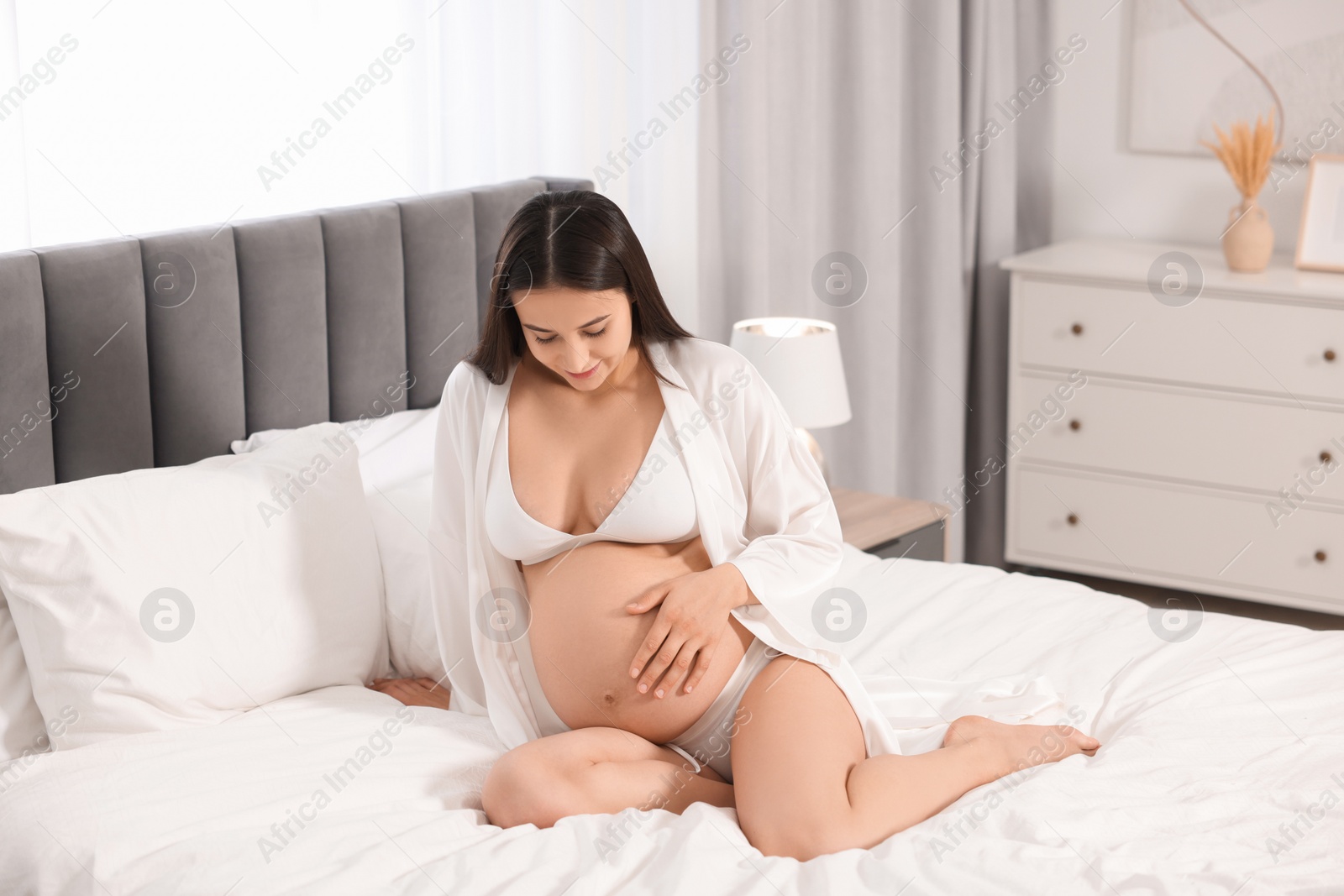 Photo of Beautiful pregnant woman in stylish comfortable underwear and robe on bed at home