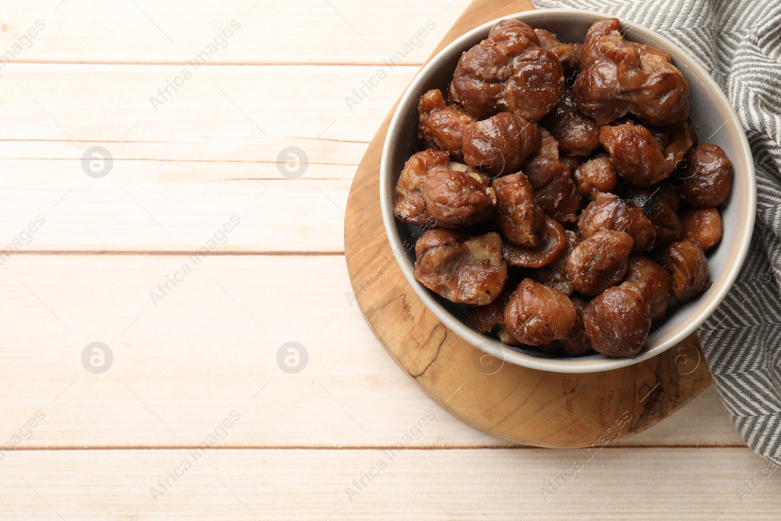 Photo of Roasted edible sweet chestnuts in bowl on light wooden table, top view. Space for text