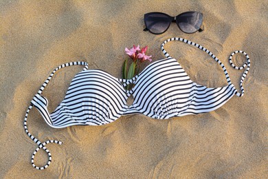 Photo of Beautiful sunglasses, swimsuit and tropical flower on sand, above view