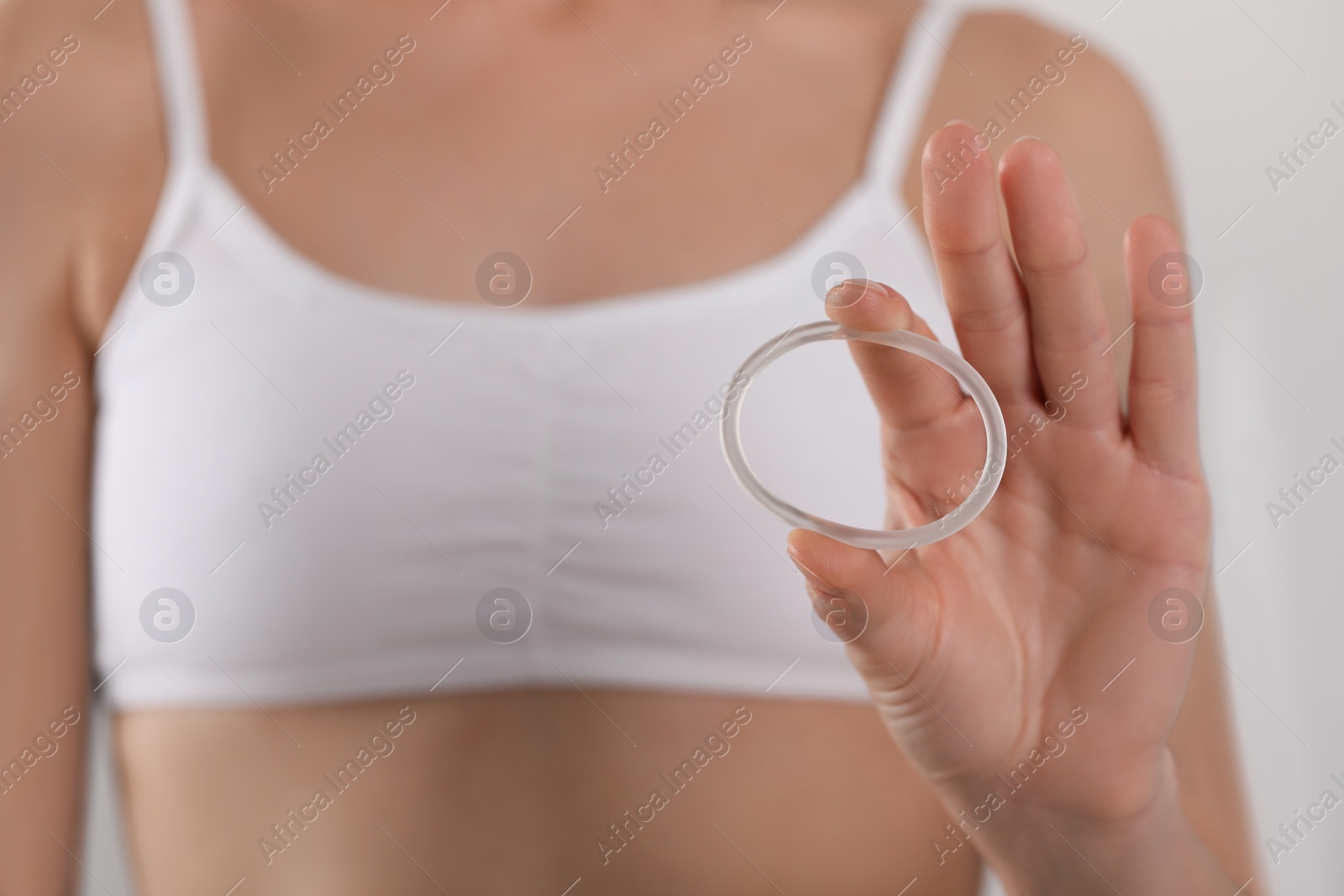 Photo of Woman holding contraceptive diaphragm (vaginal ring) on light grey background, closeup