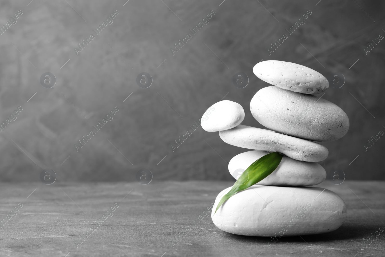 Photo of Stack of zen stones and bamboo leaf on table against grey background. Space for text