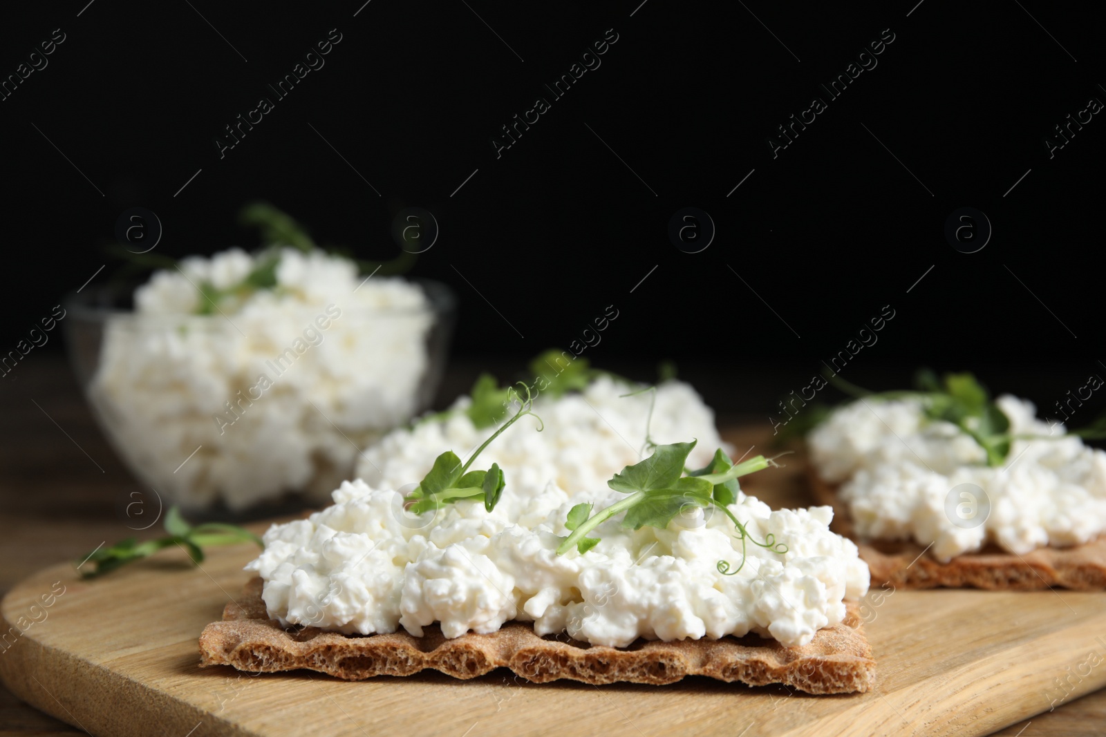 Photo of Crispy crackers with cottage cheese and microgreens on wooden board, closeup