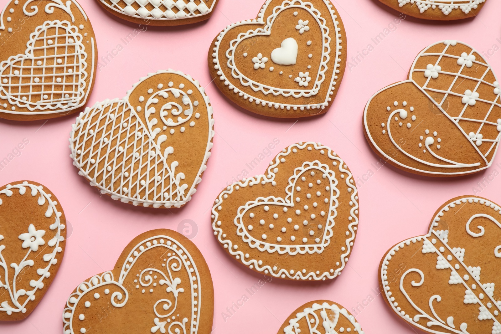 Photo of Gingerbread hearts decorated with icing on pink background, flat lay