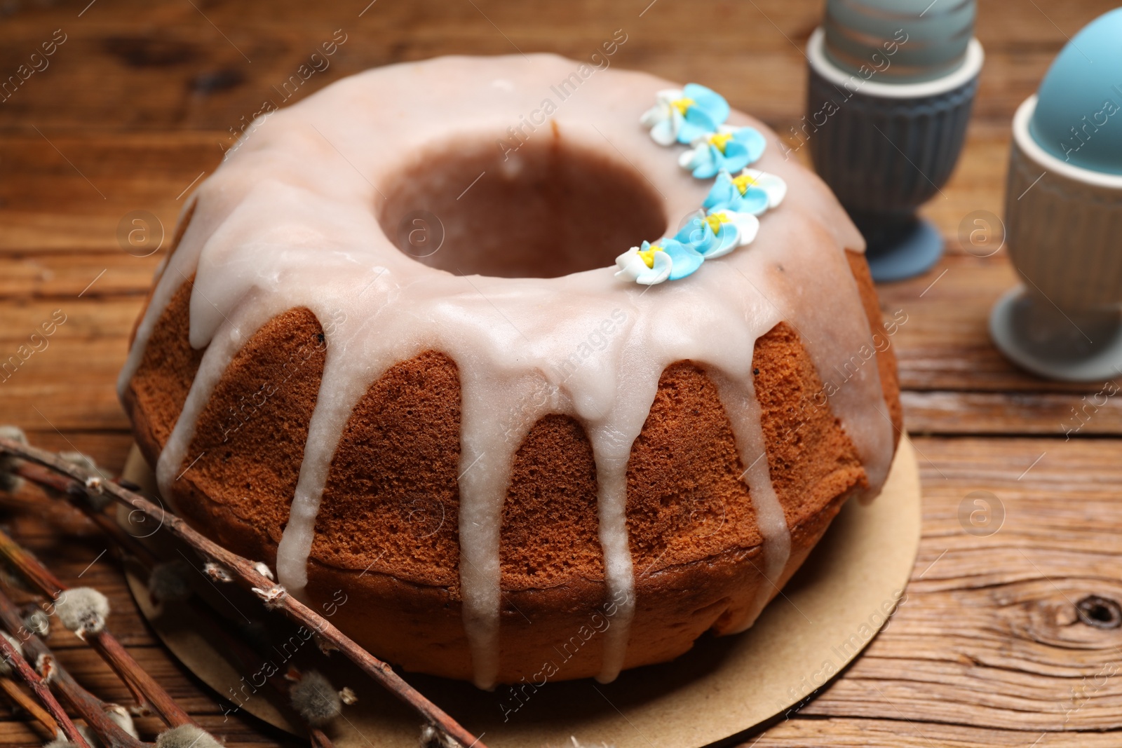 Photo of Delicious Easter cake decorated with sprinkles near willow branches and painted eggs on wooden table, closeup