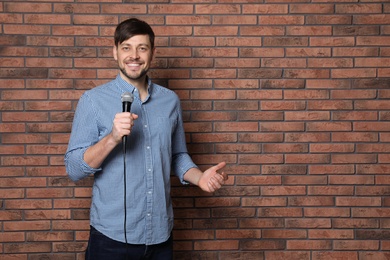 Handsome man in shirt with microphone near brick wall. Space for text