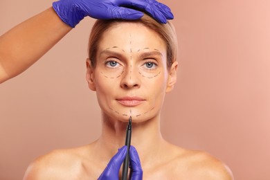 Photo of Doctor with marker preparing patient for cosmetic surgery operation on light brown background