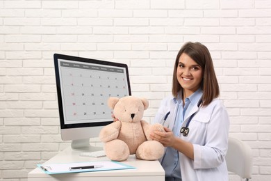 Pediatrician with teddy bear at table in clinic