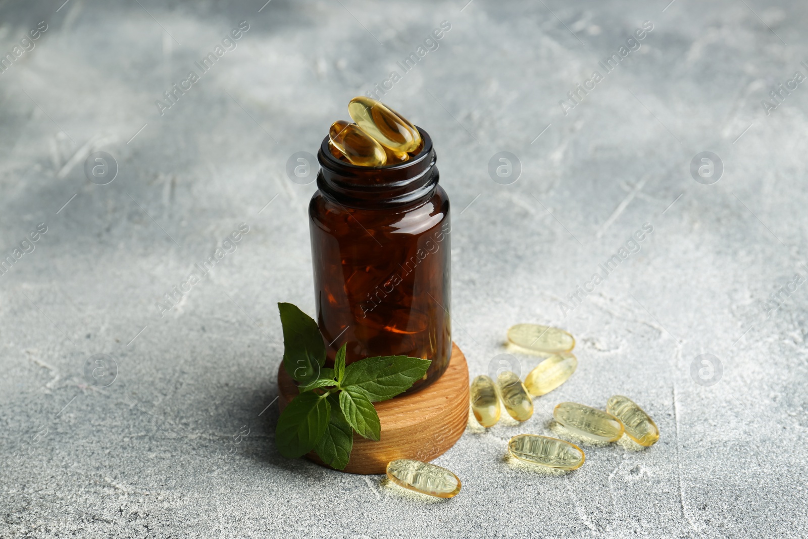 Photo of Medical bottle, mint and yellow capsules on light gray textured table