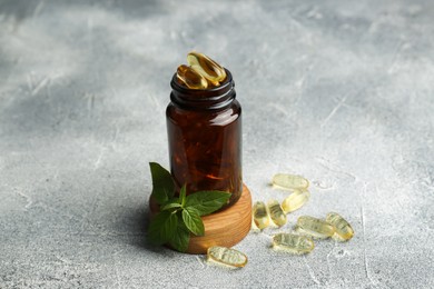 Medical bottle, mint and yellow capsules on light gray textured table