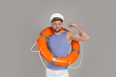 Photo of Strong sailor with orange ring buoy showing biceps on grey background