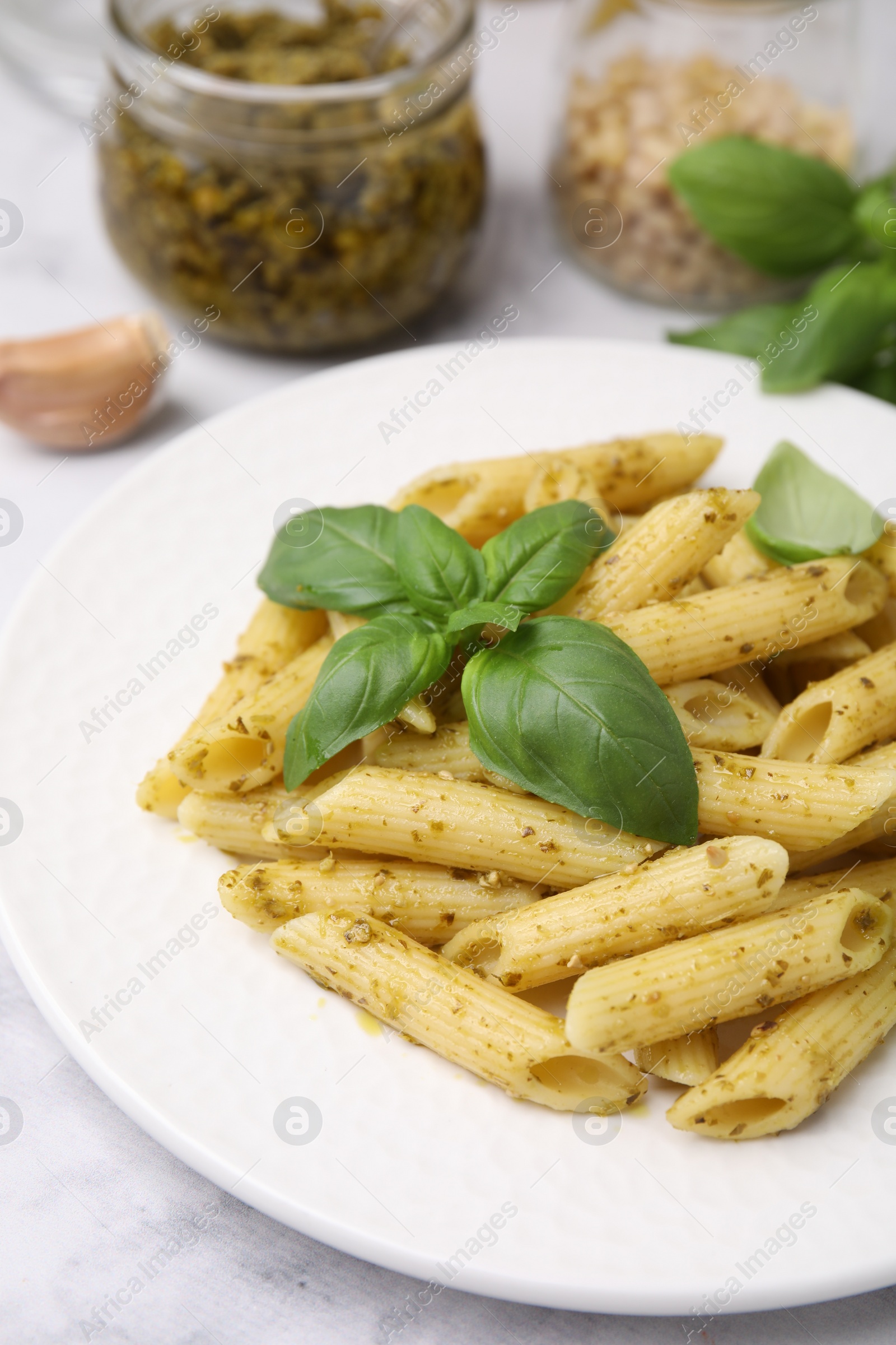 Photo of Delicious pasta with pesto sauce and basil on white marble table, closeup