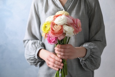 Woman holding beautiful ranunculus flowers against light blue background, closeup