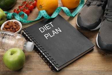 Photo of Notebook with phrase Diet Plan, sneakers and different products on wooden table