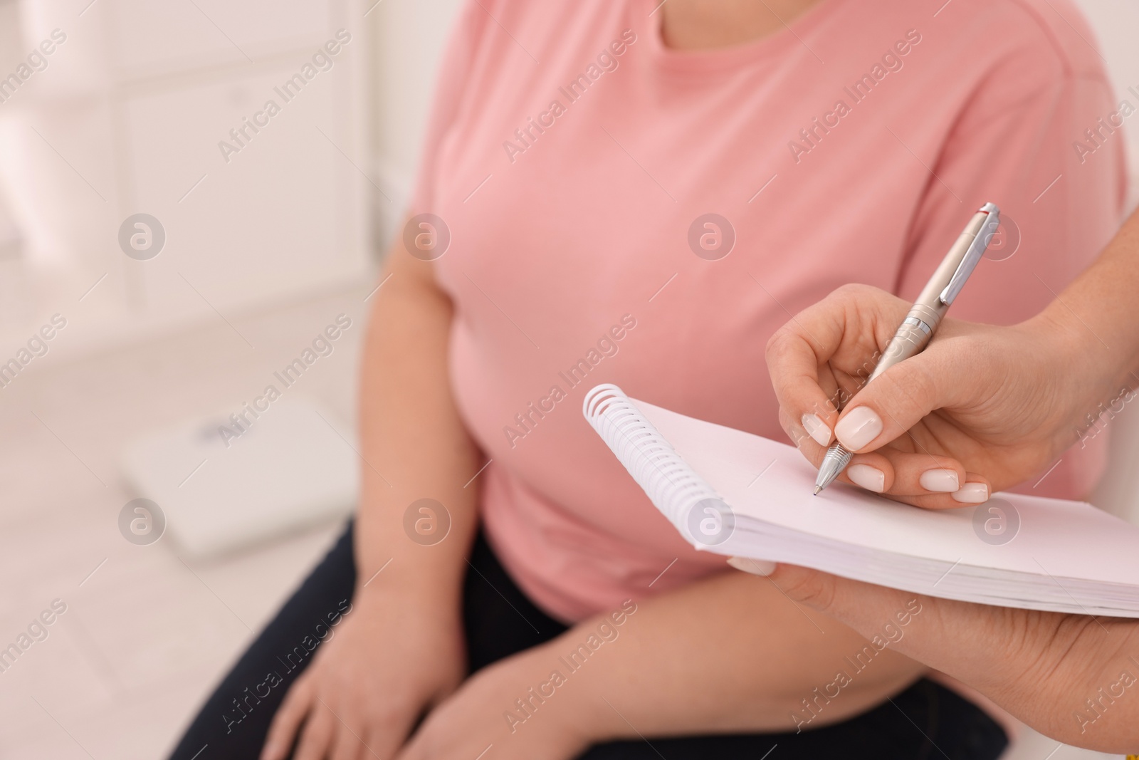 Photo of Nutritionist with notebook consulting overweight woman in clinic, closeup
