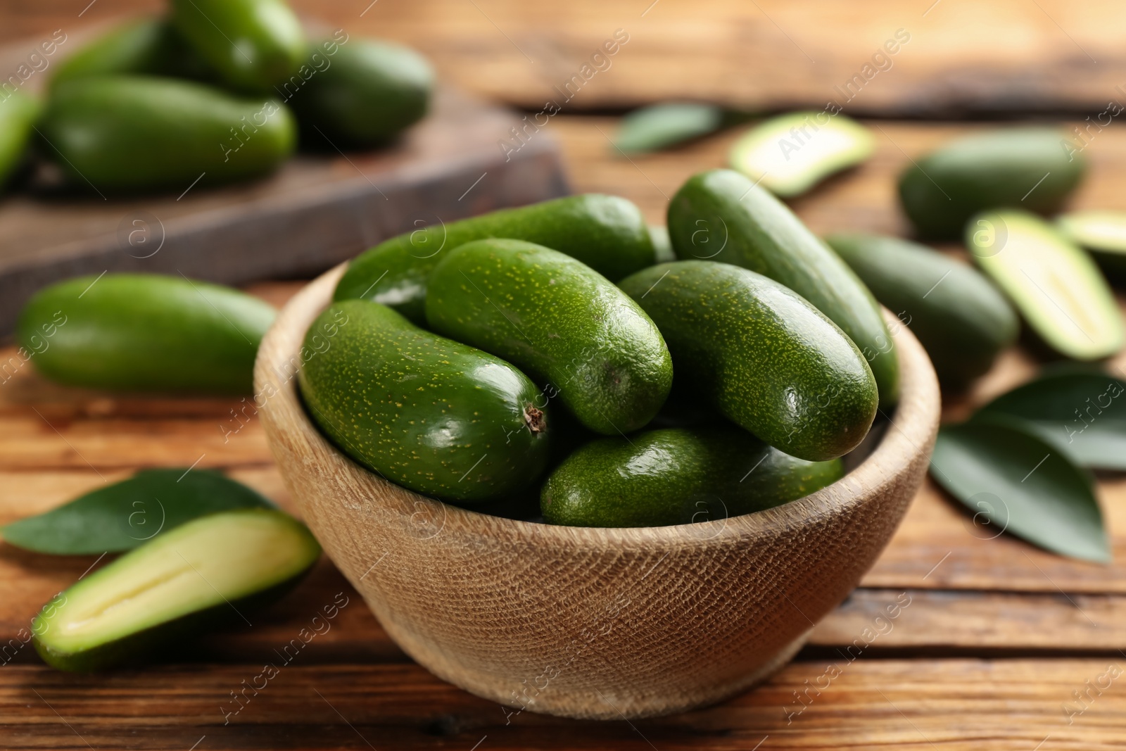 Photo of Fresh seedless avocados with green leaves in bowl on wooden table, closeup