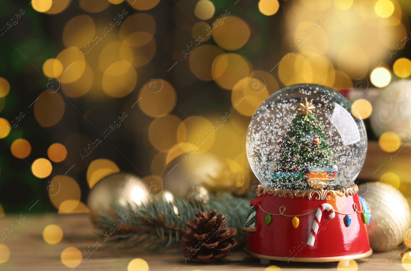 Image of Beautiful snow globe and Christmas decor on wooden table against blurred festive lights, space for text. Bokeh effect