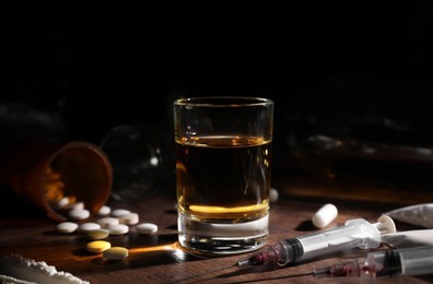 Photo of Alcohol and drug addiction. Whiskey in glass, syringes, pills and cocaine on wooden table