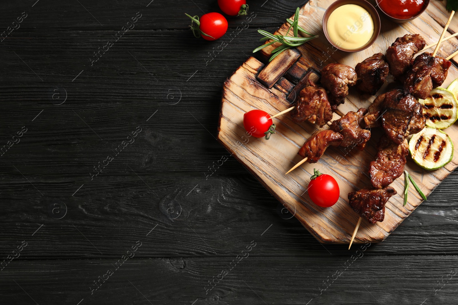 Photo of Board with barbecued meat, garnish and sauces on wooden background, top view. Space for text