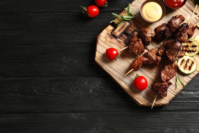 Board with barbecued meat, garnish and sauces on wooden background, top view. Space for text