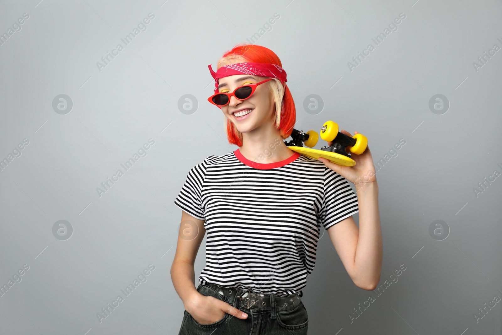 Photo of Beautiful young woman with bright dyed hair holding skateboard on light grey background