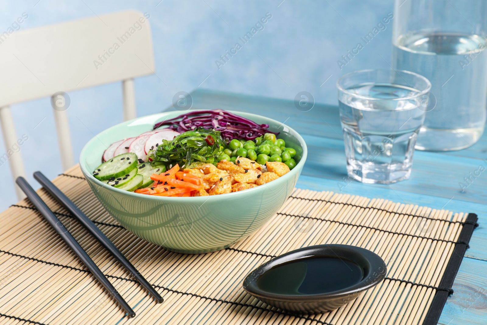 Photo of Delicious salad with chicken, vegetables and seaweed on light blue table