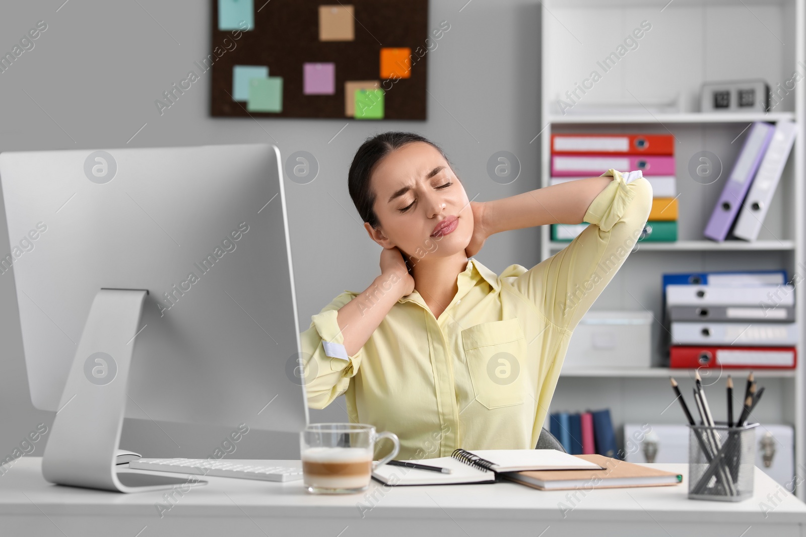 Photo of Young woman suffering from neck pain at table in office