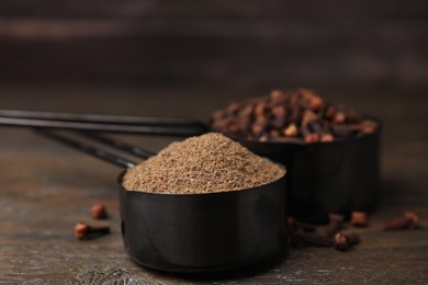 Aromatic clove powder and dried buds in scoops on wooden table, closeup