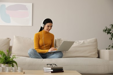 Photo of Woman with laptop and headphones sitting on sofa at home