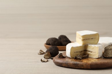 Photo of Delicious cheese and fresh black truffles on white wooden table. Space for text