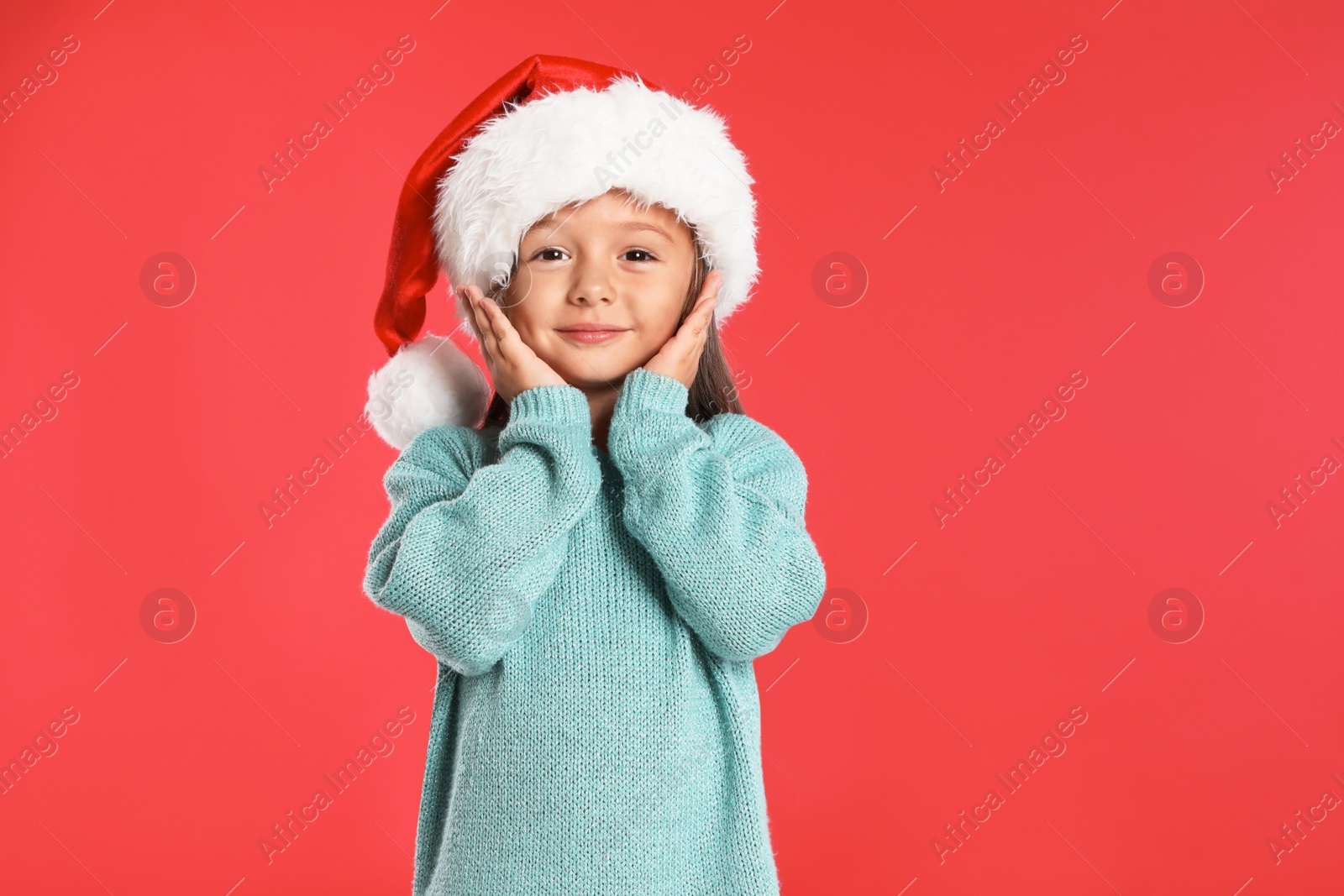 Photo of Happy little child in Santa hat on red background. Christmas celebration