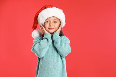 Happy little child in Santa hat on red background. Christmas celebration