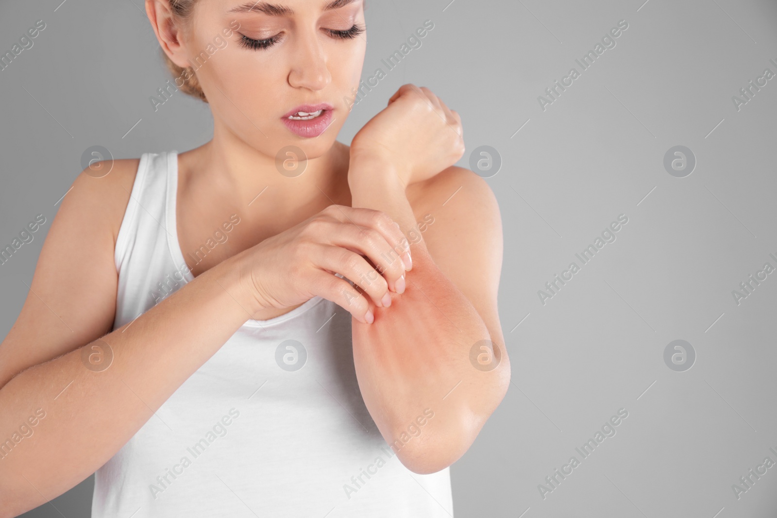 Photo of Woman scratching forearm on grey background, space for text. Allergy symptoms
