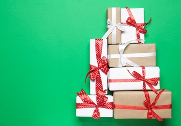 Photo of Christmas tree shape of gift boxes on green background, flat lay. Space for text