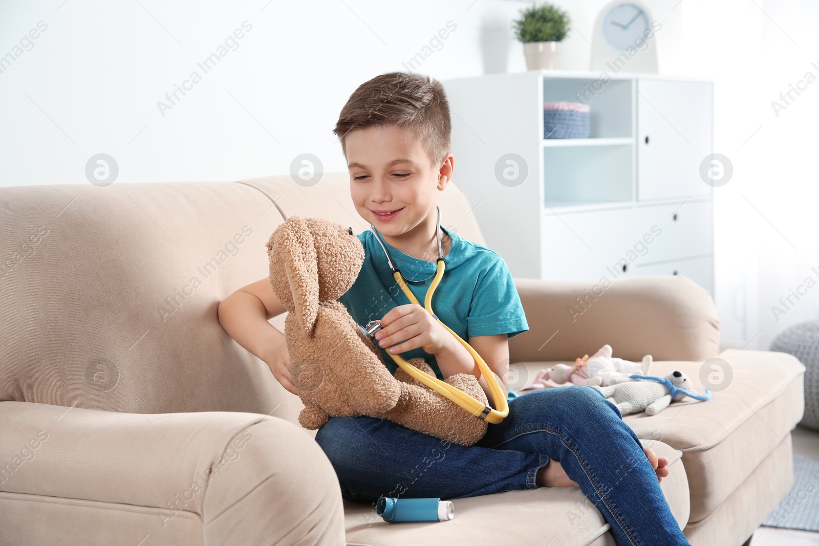 Photo of Cute child imagining himself as doctor while playing with stethoscope and toy bunny at home