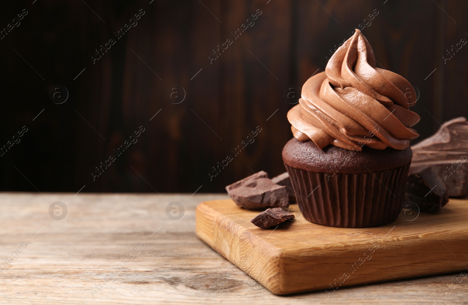 Photo of Delicious cupcake with cream and chocolate pieces on wooden table, closeup. Space for text