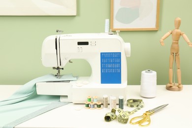 Photo of Modern sewing machine with cloth and craft accessories on white table near light green wall