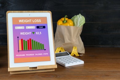 Photo of Tablet with weight loss calculator application and food products on wooden table, space for text