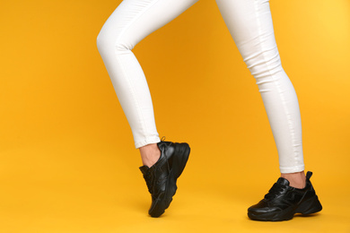 Woman wearing stylish sneakers on yellow background, closeup