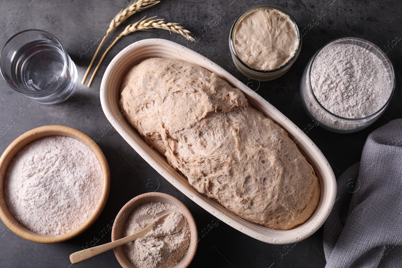 Photo of Fresh sourdough, flour, water and spikes on grey table, flat lay