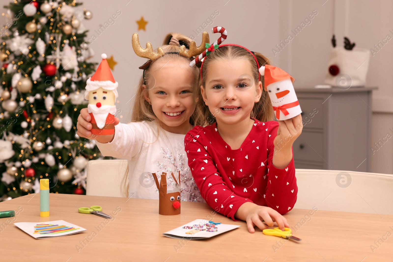 Photo of Cute little children with beautiful Christmas crafts at table in decorated room