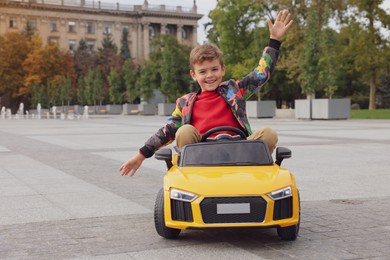 Cute little boy driving children's car on city street