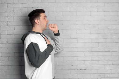 Young man coughing on brick wall background