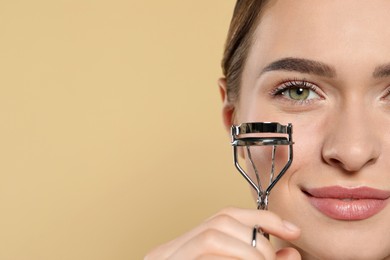 Photo of Woman with eyelash curler on beige background, closeup. Space for text