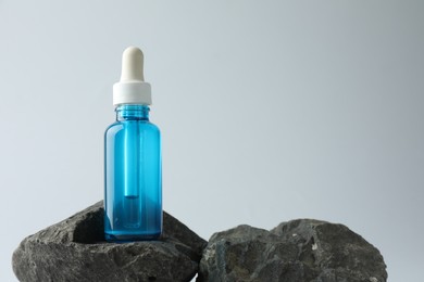 Bottle of cosmetic serum on stone against light grey background