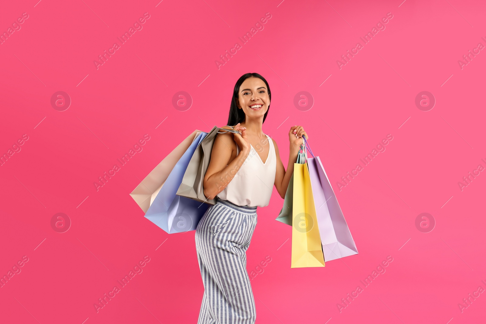 Photo of Beautiful young woman with paper shopping bags on pink background